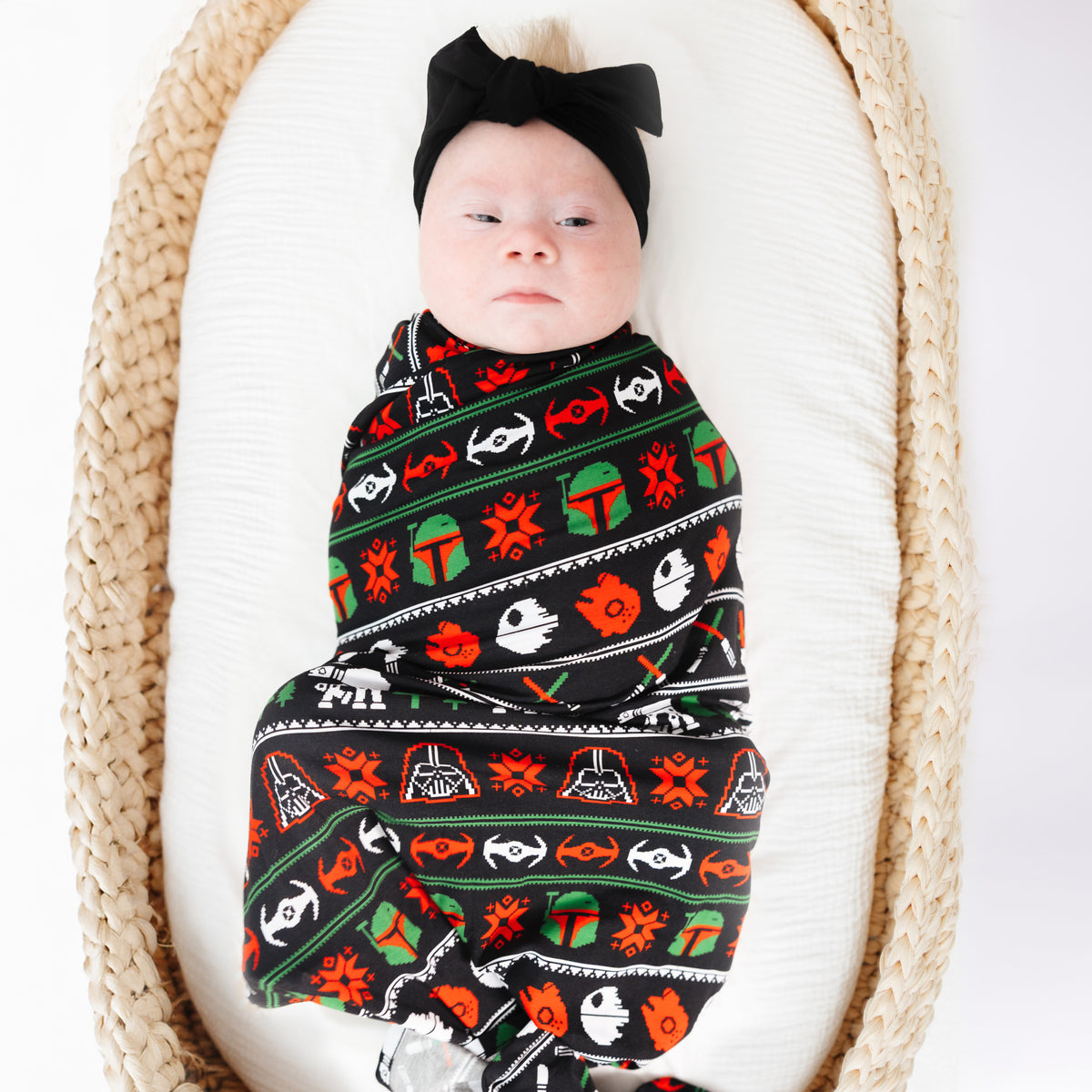 Baby in a basket wrapped in the Merry Galaxy bamboo swaddle with a black bow headband