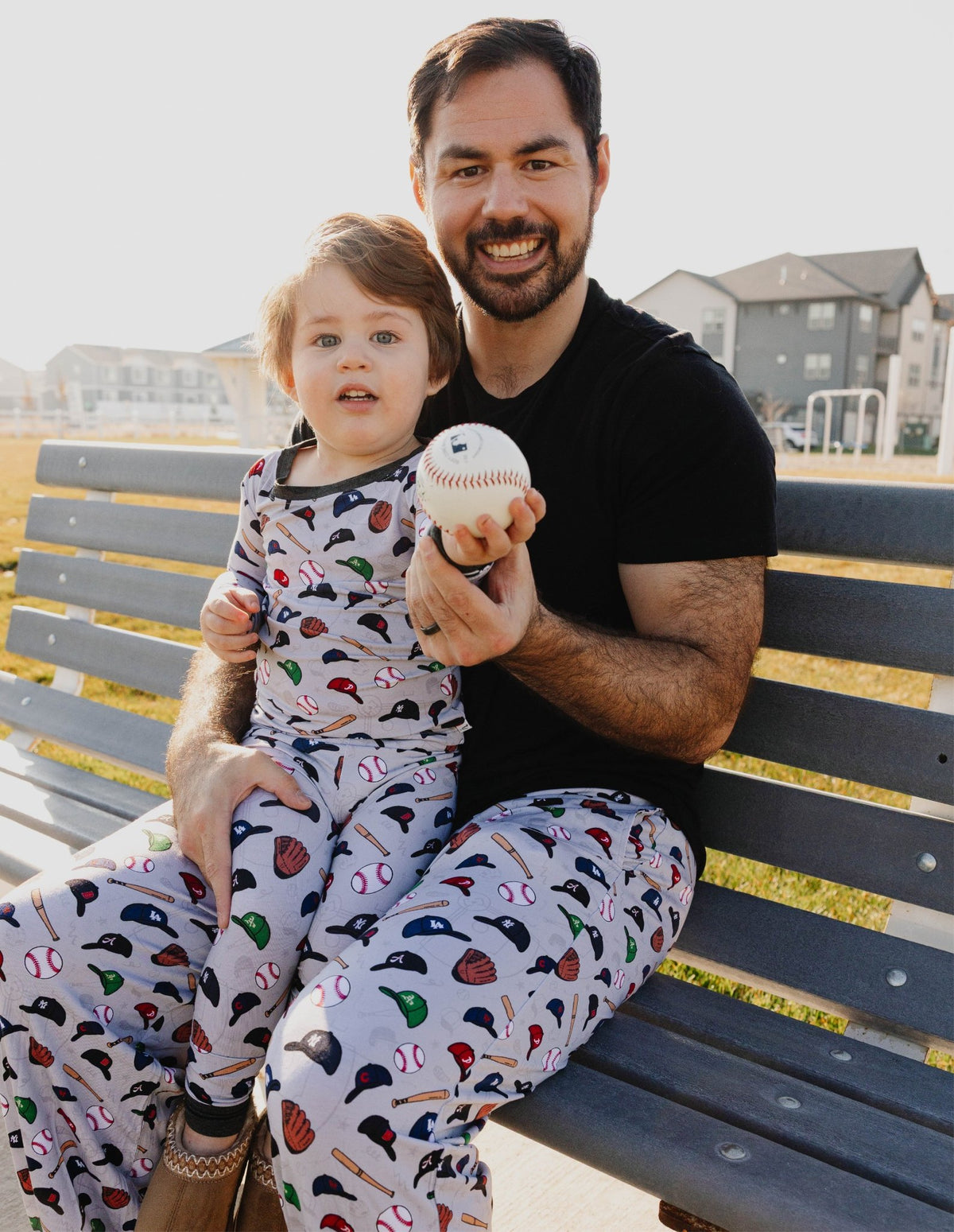 Dad and toddler matching in Major League Buddies bamboo pajamas on a park bench