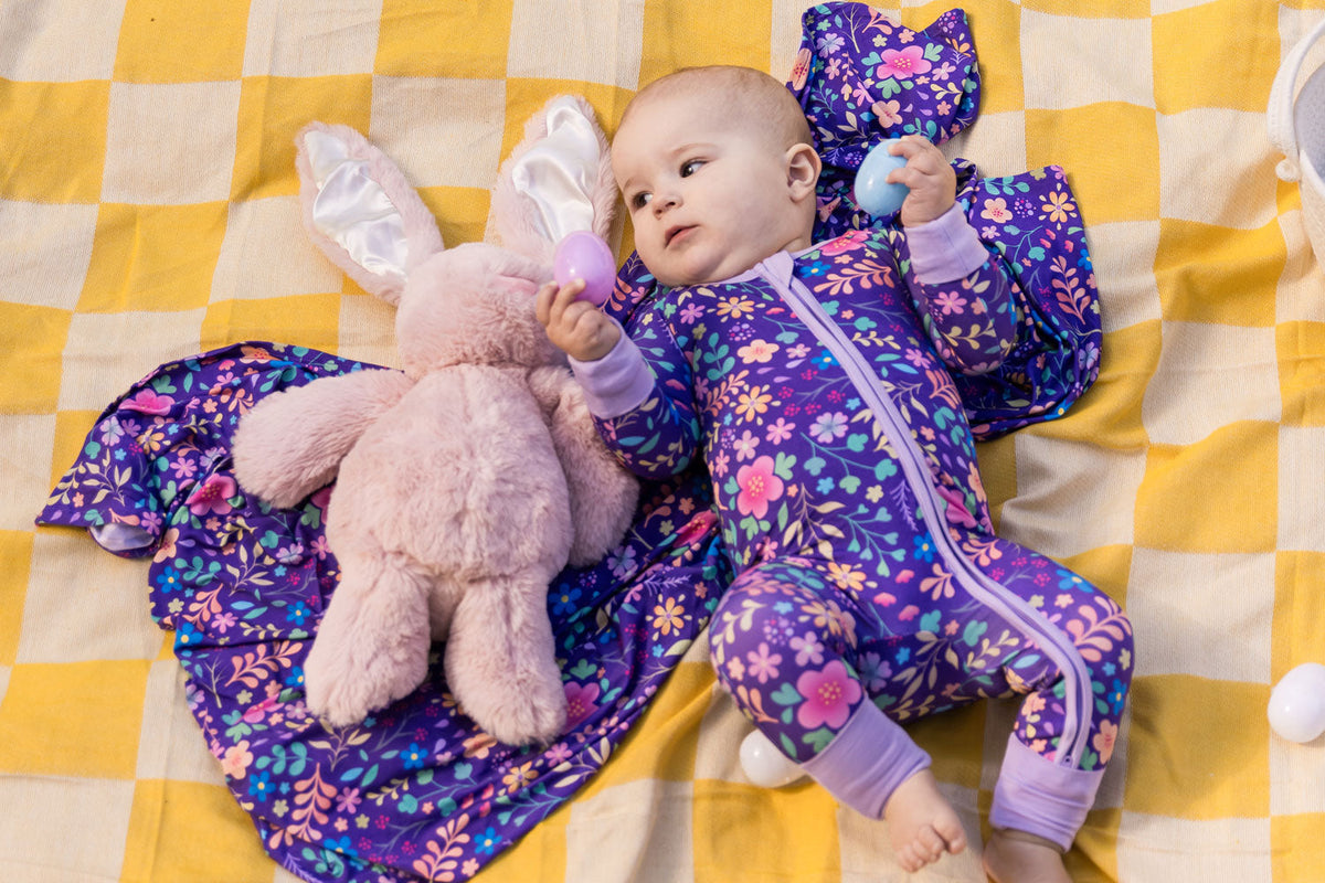 A baby wearing Bam and Stitch pajamas on a purple blanket with a stuffed animal