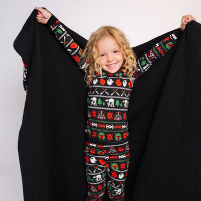Girl in Merry Galaxy pajamas holding open the blanket's black quilted side