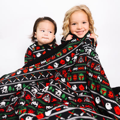 Two kids snuggled under the Merry Galaxy bamboo blanket
