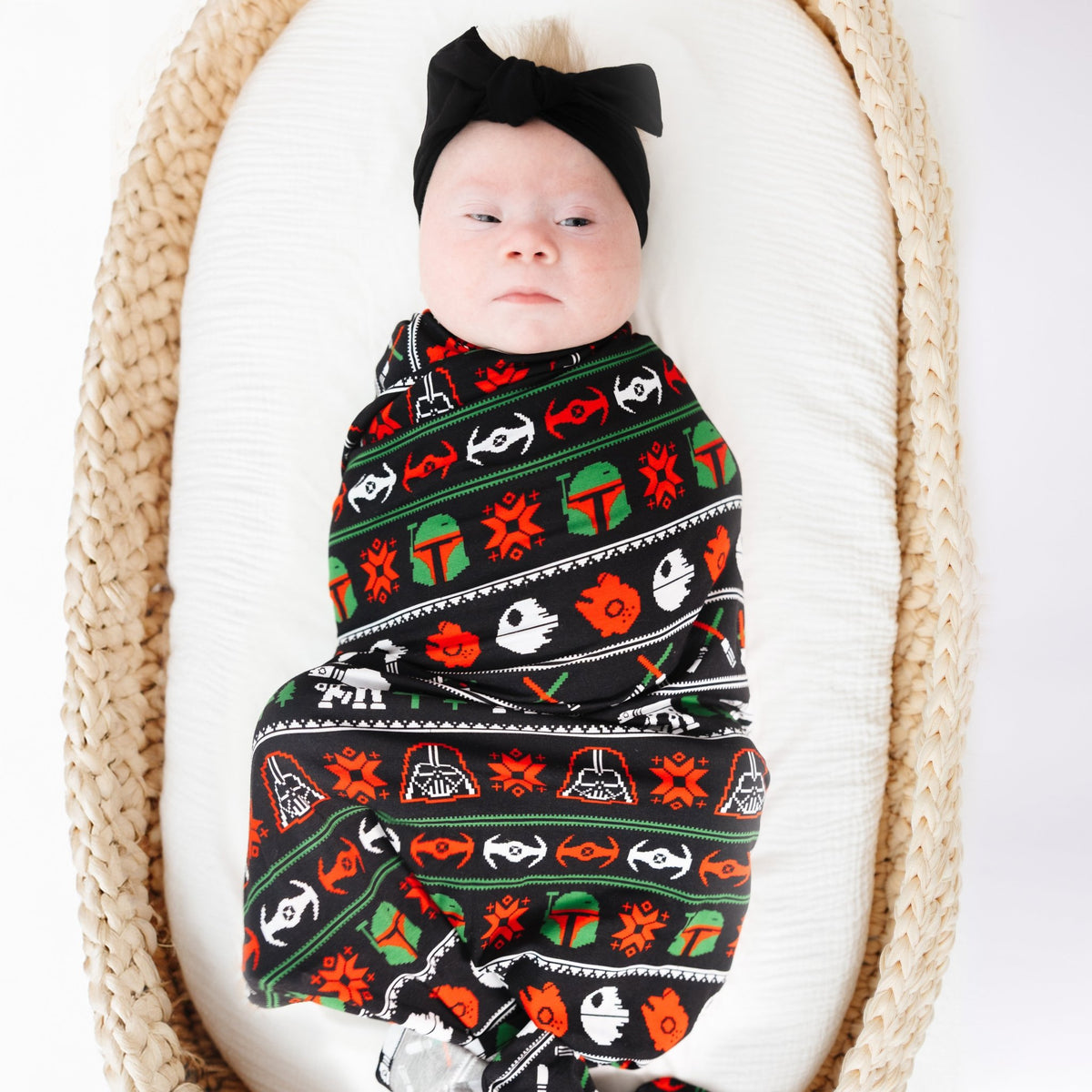 Baby in a basket wrapped in the Merry Galaxy bamboo swaddle with a black bow headband