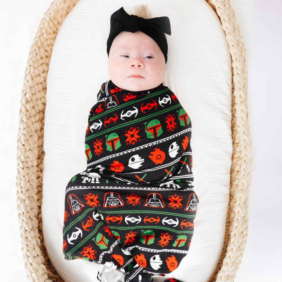 Baby in a basket wrapped in the Merry Galaxy bamboo swaddle with a black bow headband